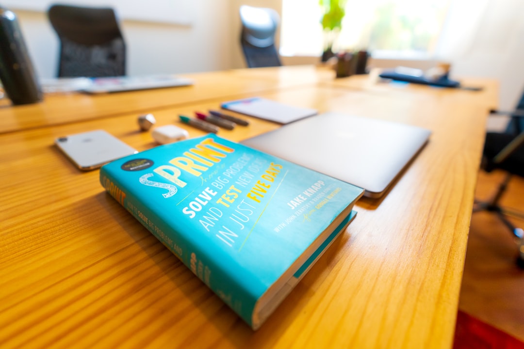 Book, a computer and other office supplies. | blue and green book on brown wooden table
