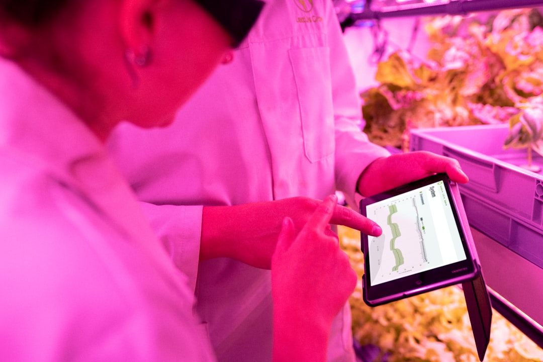 Engineers monitor crops in sustainable indoor farm | man in pink dress shirt holding black smartphone